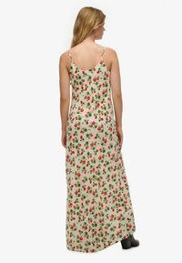 Maxi-jurk van crèmekleurige stof met rood aardbeienprint. Heeft dunne bandjes en een vloeiende silhouet die tot aan de enkels reikt.