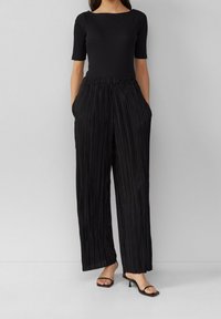 Haut noir côtelé à manches courtes associé à un pantalon large plissé noir avec taille élastique et poches latérales. Talons noirs à lanières.