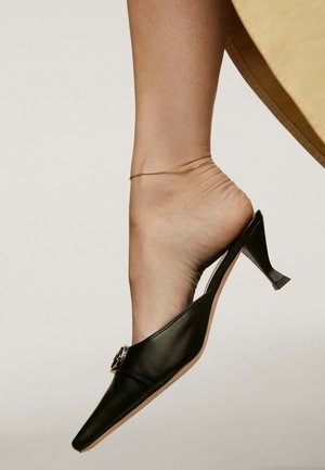 Zapato slingback de cuero negro con punta afilada y tacón pequeño. Presenta una hebilla decorativa de plata en la parte delantera y una textura suave.