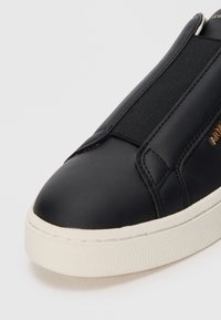 Sneaker in pelle nera con pannelli elasticizzati, punta rotonda e suola in gomma di colore crema texturizzato. Presenta un design minimalista e una targhetta dorata.