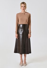 Maglietta marrone a maniche lunghe con un leggero taglio sulle spalle, abbinata a una gonna midi in pelle nera caratterizzata da una texture liscia e dettagli delle cuciture.
