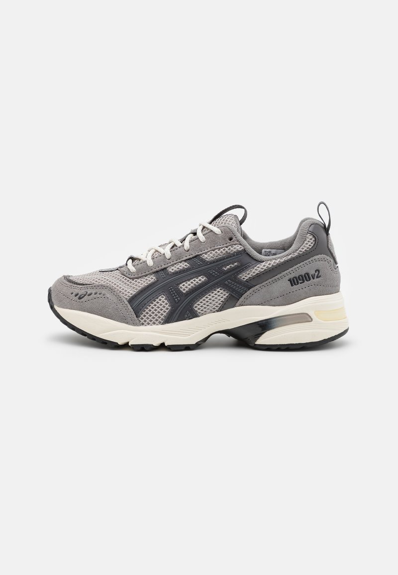 Grijze sport schoen met een bovenkant van mesh en suède, zwarte accenten, witte veters, rubberen zool en een lichte hak. Modelnummer 1090v2 aan de zijkant.