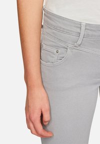 Jeans in denim grigio chiaro con design a cinque tasche, dotati di una piccola tasca frontale e dettagli in metallo argentato sui bordi delle tasche.