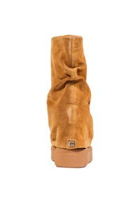 Stivale alla caviglia in suede tan con design arricciato, punta tonda e suola in gomma. Presenta un piccolo accento metallico sul retro.