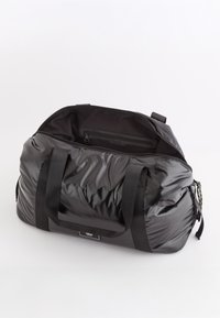 Czarna torba sportowa o błyszczącej, wyprofilowanej powierzchni, z podwójnymi mocnymi uchwytami i kieszenią na zamek wewnątrz. Posiada fakturowaną powierzchnię.