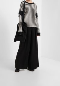 Randig tröja i grått och svart med långa ärmar, parat med vida svarta byxor och en stor svart toteväska. Mjuk, strukturerad tyg.