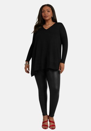 Top nero a maniche lunghe con scollo a V abbinato a leggings neri lucidi. La modella indossa sandali rossi, che evidenziano un fit rilassato e una texture morbida.