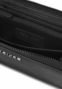 Portefeuille noir avec fermeture éclair, en cuir texturé, comportant plusieurs compartiments, doublure en tissu et un logo subtilement embossé sur une étiquette.