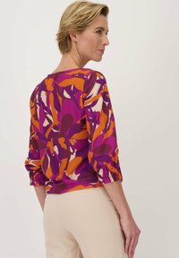 Kleurrijke blouse met een bloemenpatroon in paars, oranje en crème, met driekwartmouwen en gathered manchetten.