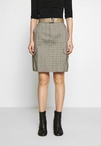 Jupe à carreaux gris avec deux poches latérales, taille haute et large ceinture beige. Portée avec des bottines noires, le tissu semble texturé.