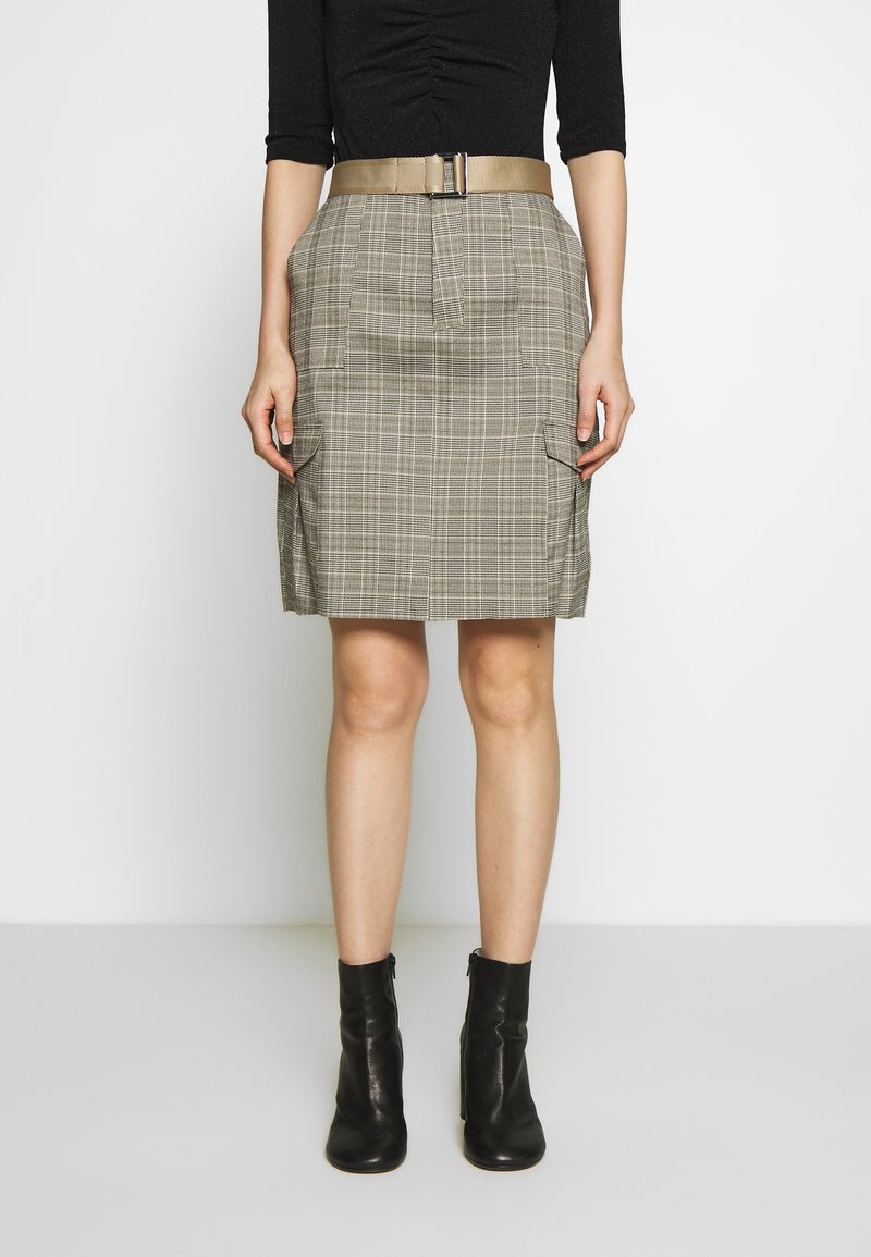Jupe à carreaux gris avec deux poches latérales, taille haute et large ceinture beige. Portée avec des bottines noires, le tissu semble texturé.