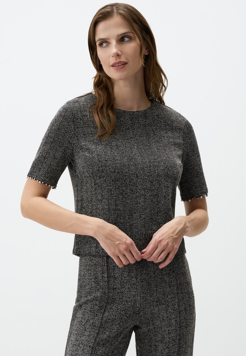 Top grigio a maniche corte con motivo houndstooth, colletto girocollo e rifiniture decorative alle maniche. Tessuto liscio, design aderente.