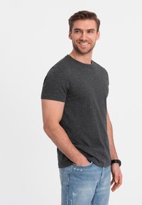 Mørkegrå kortærmet t-shirt med en tekstureret overflade, der har små farvede striber. Kombineret med lyseblå slidte jeans.