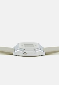 Montre numérique argentée avec un cadran rectangulaire, bracelet gris clair et un bouton sur le côté. Présente une surface plate et lisse.