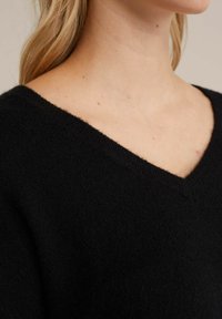 Maglione nero lavorato a maglia con scollo a V e tessuto morbido e testurizzato. Il design è semplice, con una vestibilità morbida e senza ulteriori dettagli.