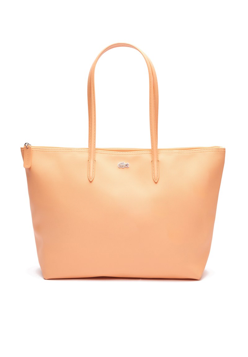 Bolso tote de color durazno hecho de material sintético suave, con dos asas largas, cierre de cremallera y un pequeño logotipo en la parte frontal.