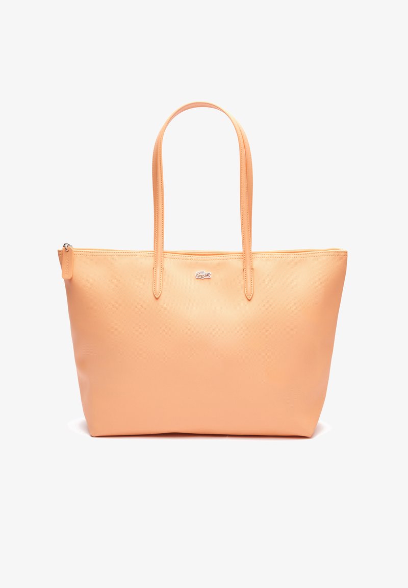 Bolso tote de color durazno hecho de material sintético suave, con dos asas largas, cierre de cremallera y un pequeño logotipo en la parte frontal.