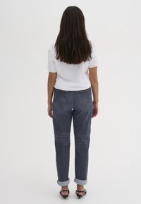 Jeans in denim blu scuro con vestibilità rilassata, orlo risvoltato e due tasche posteriori, abbinati a una t-shirt bianca semplice.