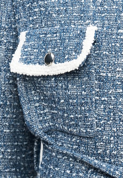 Μπλε και λευκό υφασμάτινο τουίντ με υφή, με ασημένιο κουμπί και λευκό περιμετρικό κορδόνι σε πτερύγιο τσέπης σακακιού.