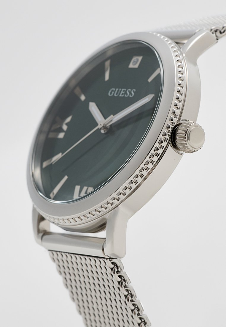 Montre avec bracelet en maillage argenté, cadran vert foncé, fenêtre de date et lunette texturée. Comprend des marqueurs d'heure et des aiguilles effilées.