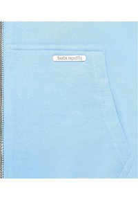 Light blue sweater with a zip closure, featuring a front pocket and a metal logo accent. Soft fabric with a smooth texture.