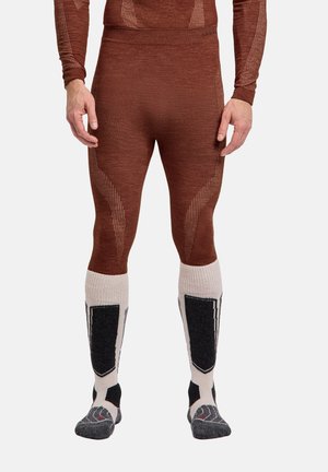 Person trägt braune, enganliegende Leggings und beige, schwarze sowie graue knielange Socken und steht vor einem schlichten Hintergrund.