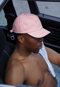 Rosa Baseballmütze aus Baumwolle, mit einer runden Krone und einem gebogenen Schirm. Die Person trägt ein Hemd über einer Schulter und sitzt in einem Auto.