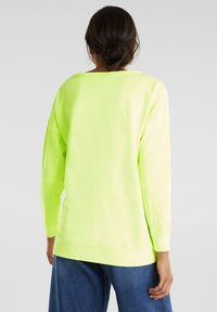 Sudadera de gran tamaño en verde neón con mangas largas, escote redondeado y puños de canalé. Textura suave, diseño casual.