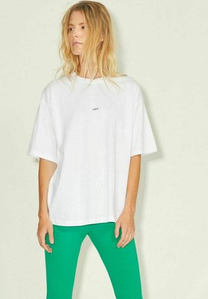 Weißes, übergroßes T-Shirt mit kurzen Ärmeln und bedrucktem Logo auf der Brust. Kombiniert mit grünen Leggings, die eine glatte Stoffstruktur aufweisen.