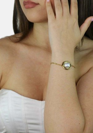 Gouden kettinkje armband met een opvallende ronde parel in het midden. Soepele textuur, elegant ontwerp en subtiele accenten in het metaalwerk.