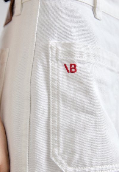 Weiße Denim-Hose mit einer Gesäßtasche, die das rot gestickte "VB"-Logo trägt. Der Stoff hat ein glattes, strukturiertes Erscheinungsbild und sichtbare Nähte.