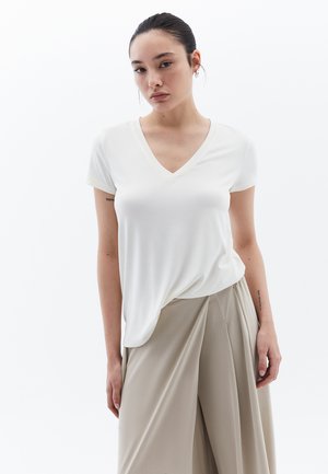 Witte T-shirt met korte mouwen en V-hals, gemaakt van zachte stof, met een ontspannen pasvorm. Gepaard met beige wijde broek voor contrast.