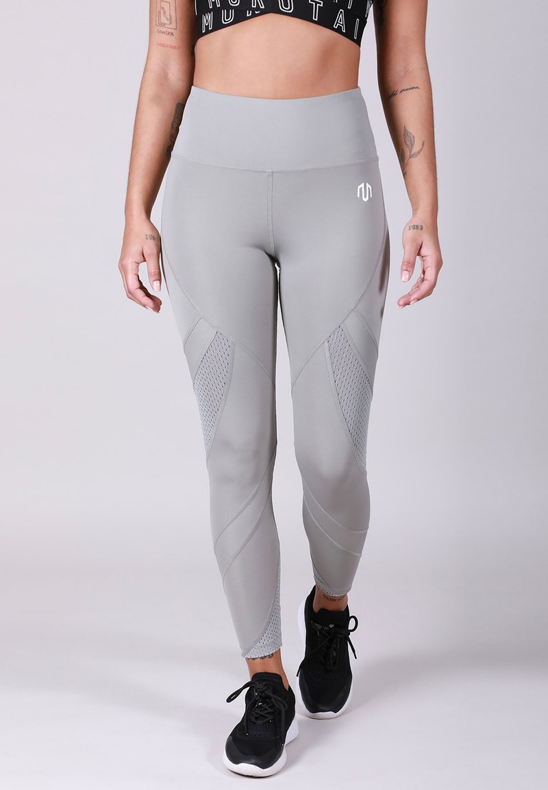 Collants de sport gris avec des panneaux en mesh, taille haute et design ajusté. Associés à des baskets noires, présentant un look sportif.