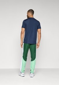 Tricou de bumbac cu mânecă scurtă de culoare bleumarin, asortat cu pantaloni de trening verzi și mentă, având panouri laterale și accente albe. Design sportiv casual.
