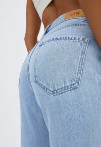 Jean en denim bleu clair avec un design à cinq poches, présentant une étiquette sur la taille et un léger délavage le long des bords.