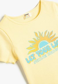 Gul ribbet kortærmet t-shirt med en blå og orange solgrafik og teksten "LAD DIT LYS STRÅLE KLART" i legende skrifttyper.