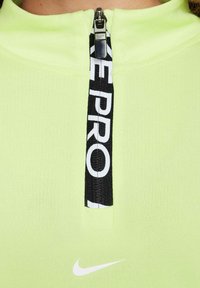 Limoengroene sporttop met een zwarte rits, een wit logo-label en een klein wit Nike-swoosh op de voorkant.