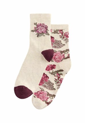 Beige katoenen sokken met bloemenpatronen in tinten van roze en groen, met bordeauxrode accentpunten op de tenen. De ene sok is bedrukt, de andere is effen.