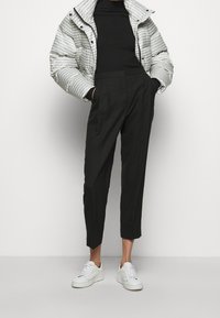 Puffjacka i grått och vitt houndstooth-mönster, kombinerad med svarta skräddarsydda byxor och vita sneakers. En klassisk, strukturerad outfit.