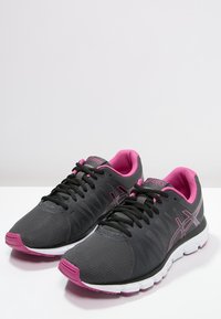 Scarpe da ginnastica grigie con accenti rosa, tomaia in rete, design testurizzato, lacci neri e suole in gomma bianca per stabilità e supporto.