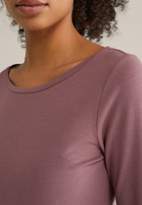 Ilgiem piedurknēm tops pelēkā mauve krāsā, ar apaļu kakla izgriezumu un gludu tekstūru. Audums izskatās mīksts un elpojošs.