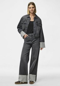 Svart denimjacka med kort längd och grå manschetter, i kombination med svarta jeans med hög midja och vida ben, som har fransade grå fållar.