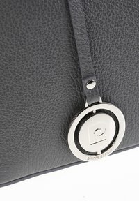 Borsa a tracolla in pelle nera con superficie texturizzata, dettaglio logo circolare argentato e una tracolla sottile attaccata nella parte superiore.