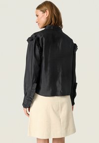 Black satin long-sleeve blouse with ruffled shoulder details and buttoned cuffs, featuring a tailored collar and mid-length cut.