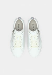 White leather sneakers with a textured surface, featuring beige laces, side zipper, and a striped accent at the heel. Gabor branding visible inside.
