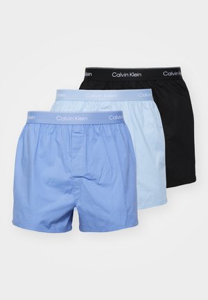 Three pairs of boxers: one light blue, one sky blue, one black. Each features a soft elastic waistband with “Calvin Klein” logo.