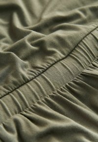 Nahaufnahme eines olivgrünen elastischen Bundes mit gerafftem, weichem Stoff an einem Kleidungsstück.