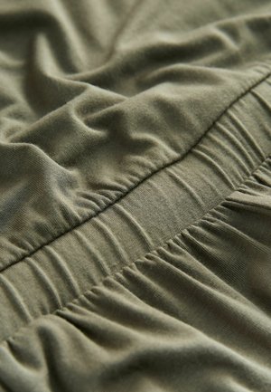 Nahaufnahme eines olivgrünen elastischen Bundes mit gerafftem, weichem Stoff an einem Kleidungsstück.