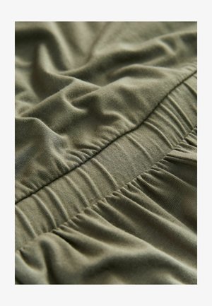 Nahaufnahme eines olivgrünen elastischen Bundes mit gerafftem, weichem Stoff an einem Kleidungsstück.