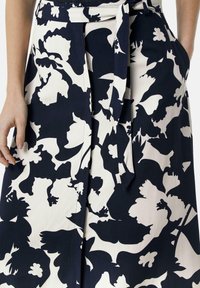Rock mit floralem Druck in Marineblau und Creme, ausgestattet mit hoher Taille, Bindegürtel und seitlichen Taschen; glatte Textur mit kontrastierenden Mustern.